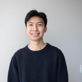 a Vietnamese young man, wearing a dark sweater and smiling at the camera