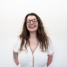 a young woman with braces and glasses and wavy brown hair smiling warmly 
