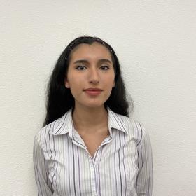 Audriana Zambrano, a Latina young woman with long, dark hair, professional attire, and a serious expression