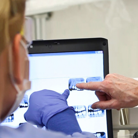 A dentist and assistant looking at dental x-rays on a screen