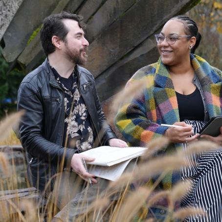 two students chat while holding notebooks and next to a fountain