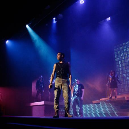 Under dramatic stage lighting, an actor gazes out into the crowd