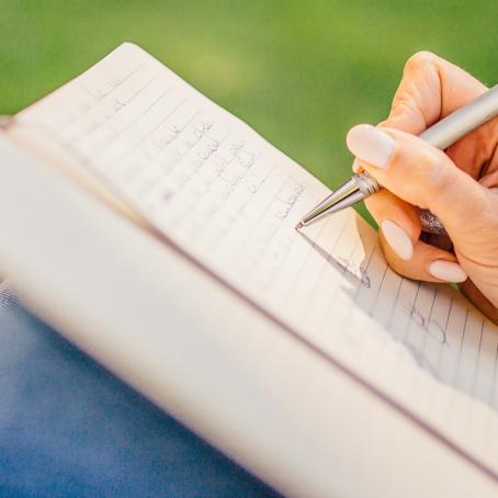 person writing on notepad propped up on their knees