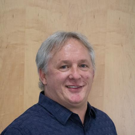 An older white man with grey hair and a shy smile