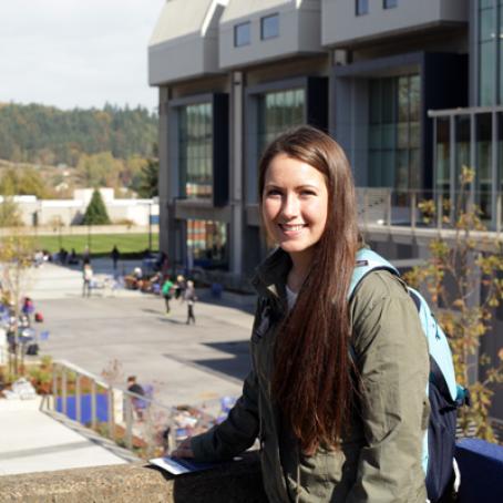 A young woman with a backpack smiling in front of Center Building on main campus