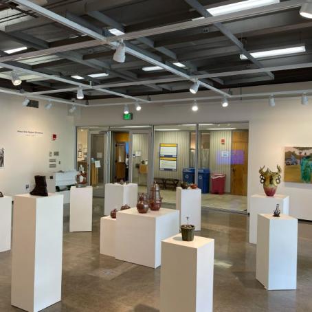 A bright art gallery room filled with student art of various mediums