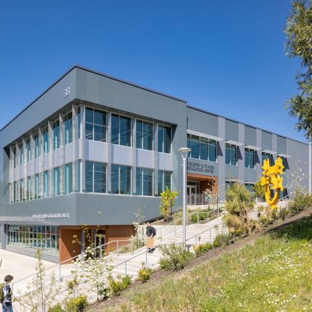 The exterior of the ITEC building on a sunny day with students and the bright yellow statue in front