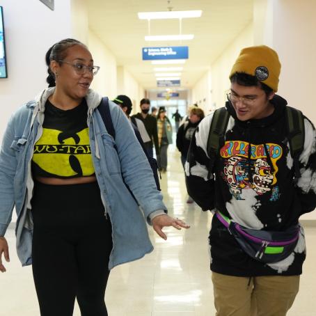 two students, a woman wearing a Wu-Tang hoodie and a man wearing a graffiti sweatshirt, smile and talk as they walk to class