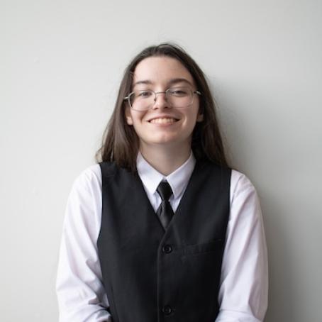 a young woman with long dark hair and glasses, wearing a vest