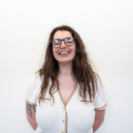 a young woman with braces and glasses and wavy brown hair smiling warmly 