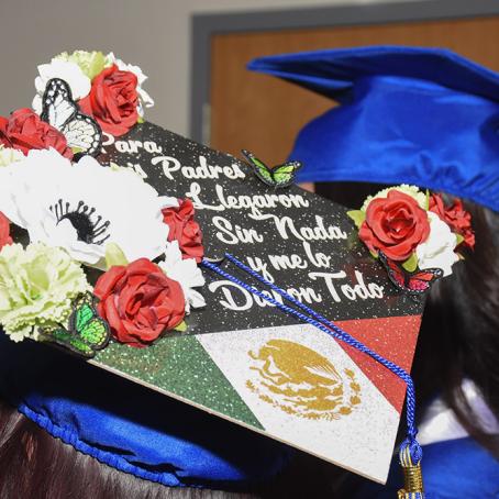 a grad cap decoratd with flowers and the Mexican flag that reads: “Para mis padres que llegaron sin nada y me lo dieron todo.”
