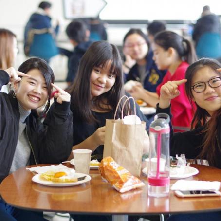 three international students sitting at a table and posing and smiling