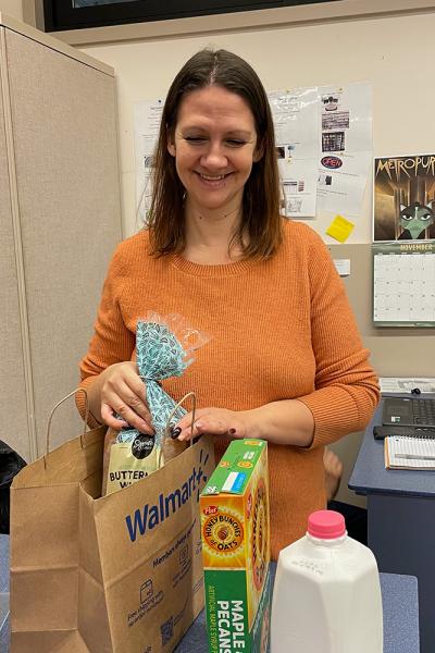 a student worker, a young woman with a gentle smile, fills a bag with bread, milk, and cereal in the Titan Pantry