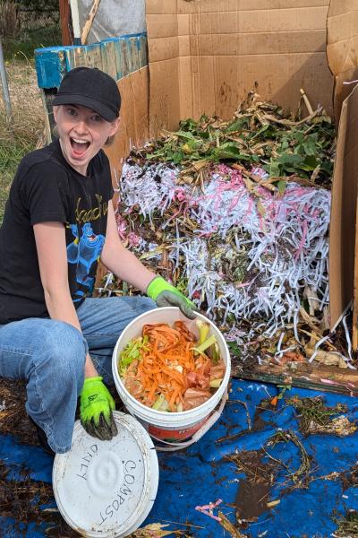 a student, a young woman in a hat, excitedly shoes off compost in a bucket in the Learning Garden