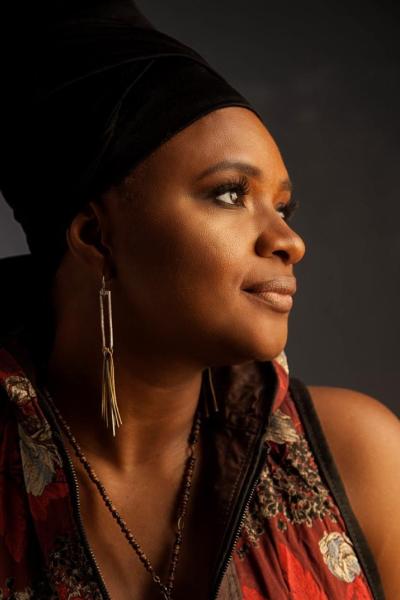 Singer Lizz Wright, a Black woman with fashionable clothes and long earrings in dramatic lighting