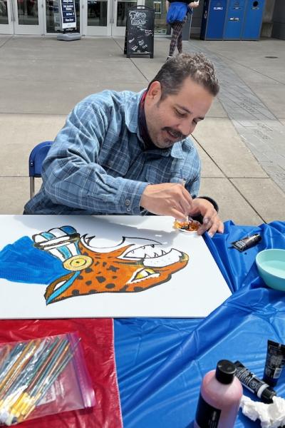 Arturo Zavala, the MEChA coordinator, painting a sign with an Aztec jaguar at a peaceful protest event on campus