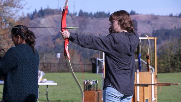 A young woman shoots an arrow from a bow on a sunny autumn day at LCC
