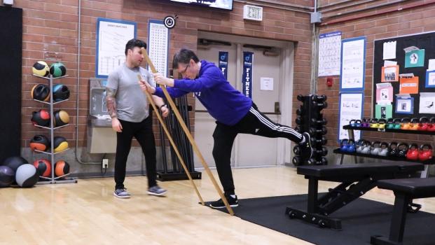 a friendly instructor helps an older student stretch in a bright, spacious fitness center