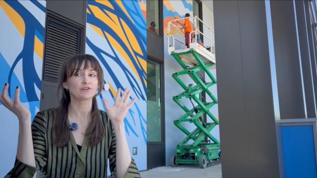 artist Jessilyn Brinkerhoff gives an interview in front of her mural