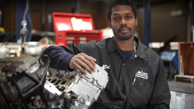 an auto tech student looks at the screen with his arm resting on a car part